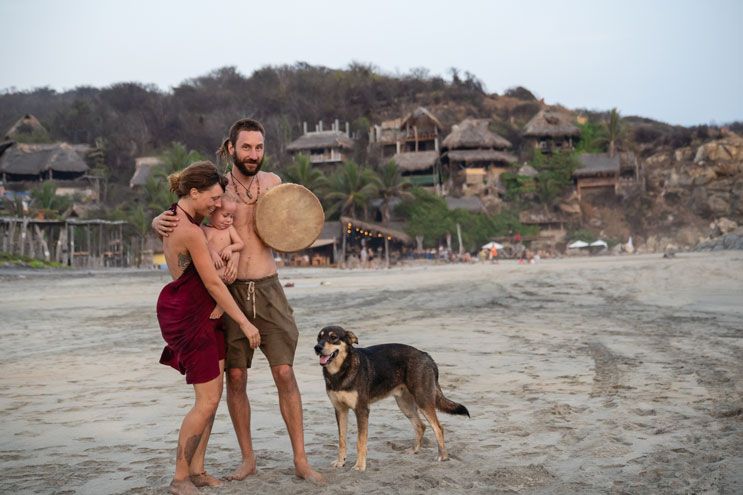 Eltern mit Neugeborenem und Hund am Strand von Mazunte vor Palmenhütten