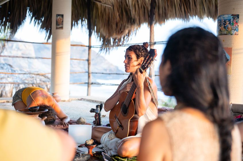 Frau spielt Gitarre in einer offenen Palapa-Hütte in Mazunte während einer Zeremonie