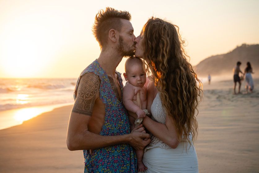 Eltern küssen sich am Strand von Mazunte und halten ihr Baby im Arm