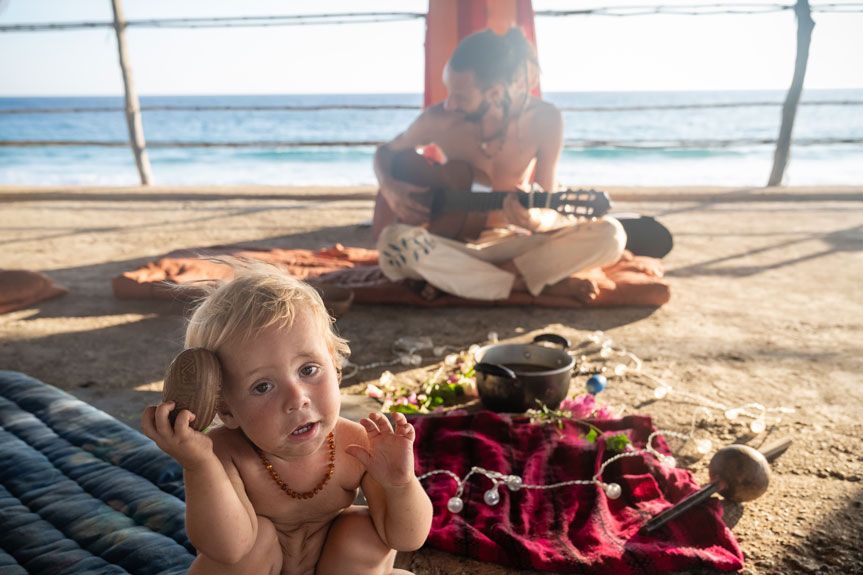 Kind mit Muschel in der Hand, im Hintergrund spielt ein Mann Gitarre am Meer in Mazunte