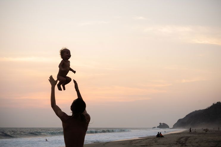 Vater wirft lachendes Kind am Strand von Mazunte in die Luft bei Sonnenuntergang